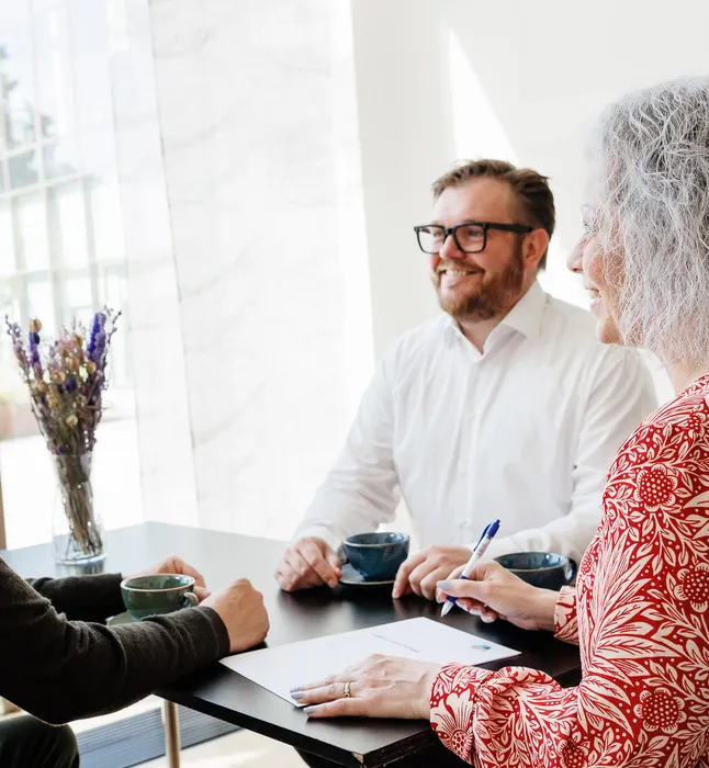 Kvinde i rød skjorte og 2 mænd holder møde